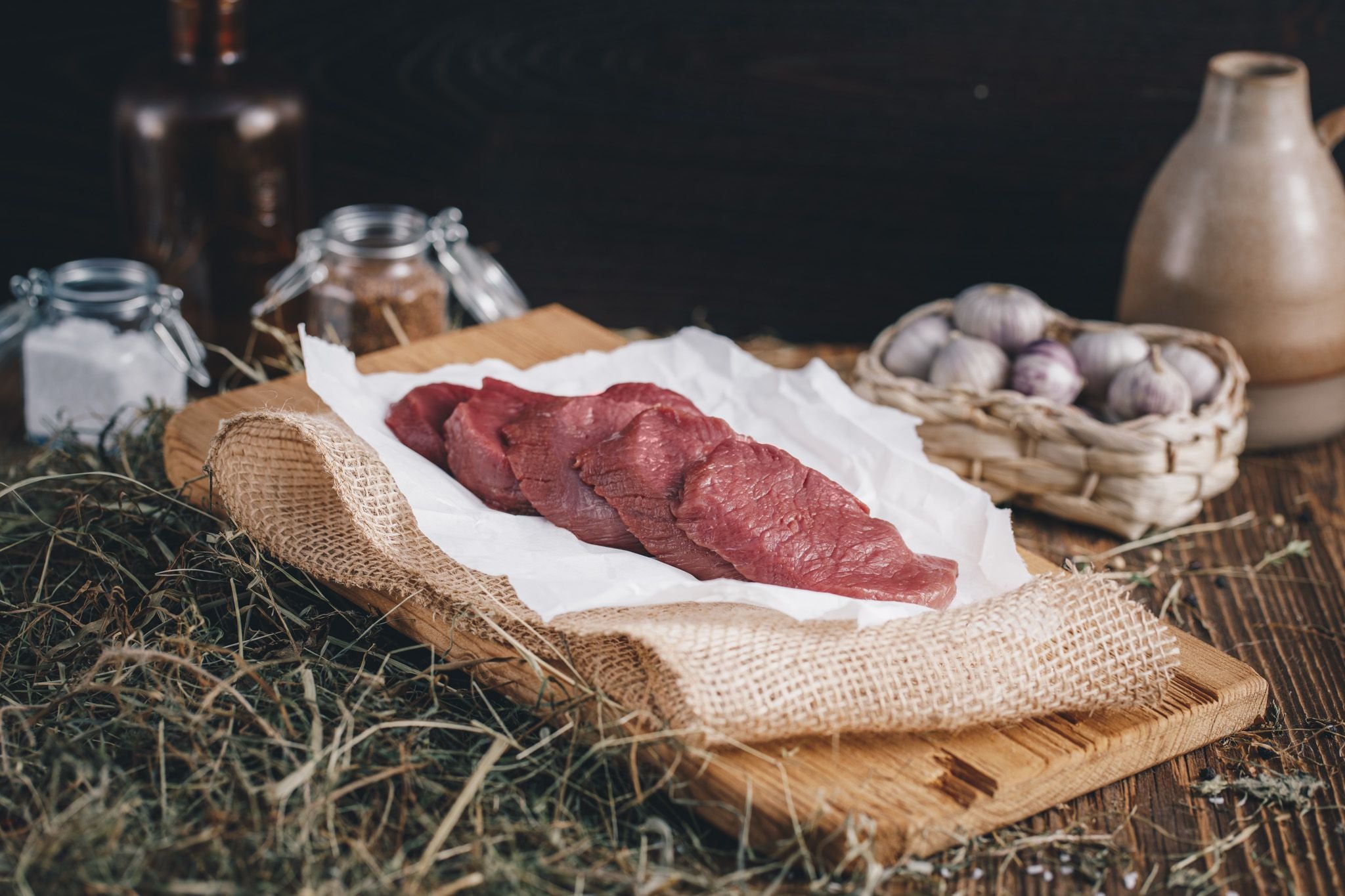 Ager Tirol Hirschfleisch Hirschschnitzel geschnitten mehrere Stück roh auf Holzbrett und Heu
